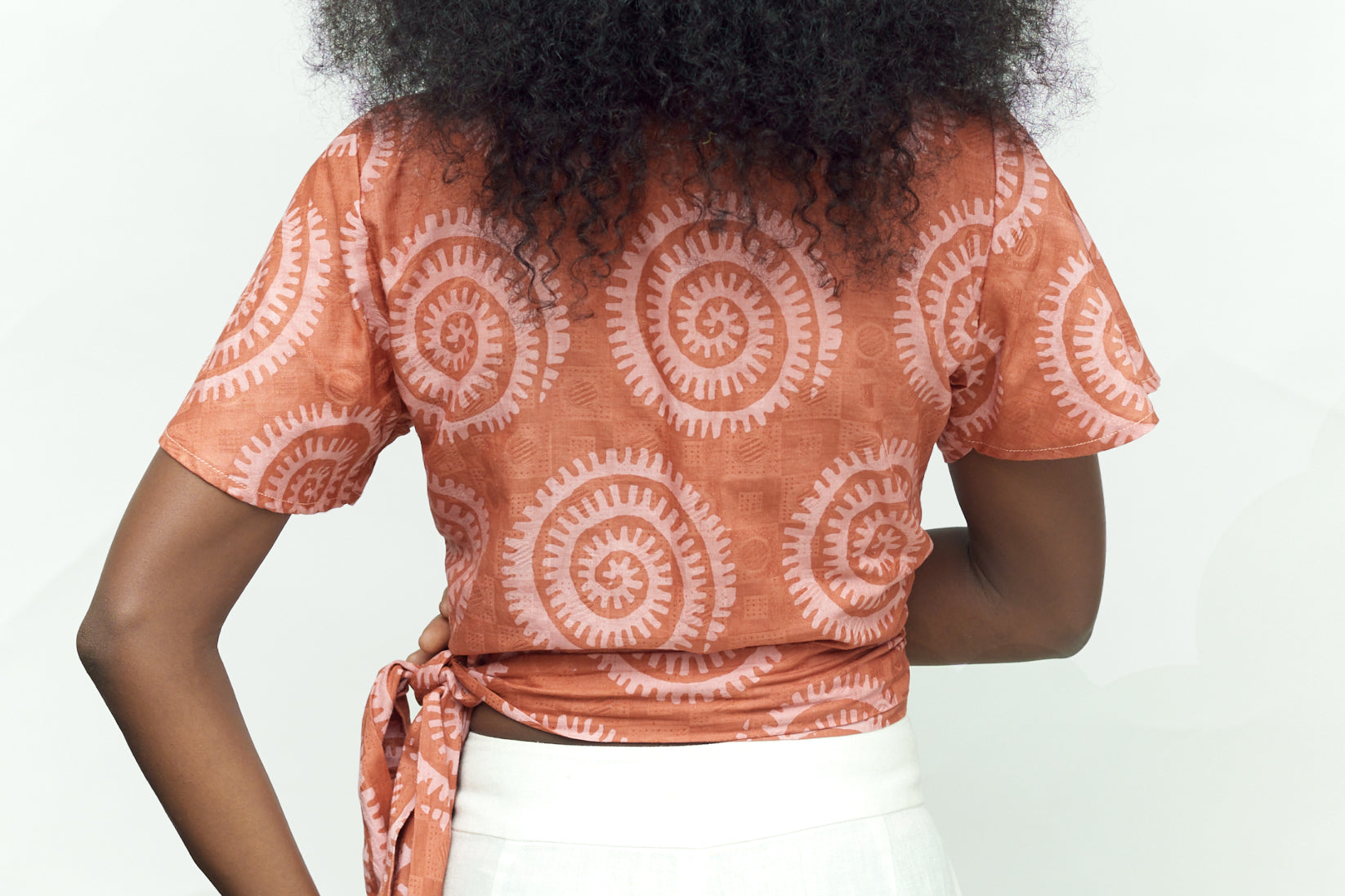 Back view of woman wearing hand-dyed pink and orange Shea Shell dot batik print Short Sleeve Wrap Top by GEOMETRIC. 