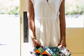 Woman wearing white dress holding three hand-dyed zipper clutch bags by GEOMETRIC. 