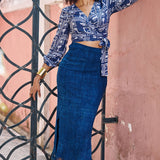 Woman wearing denim skirt and blue hand-dyed batik Coco print long sleeve wrap top by GEOMETRIC. 