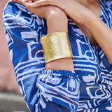 Close-up of woman wearing blue hand-dyed batik Coco print long sleeve wrap top by GEOMETRIC and brass bracelet. 