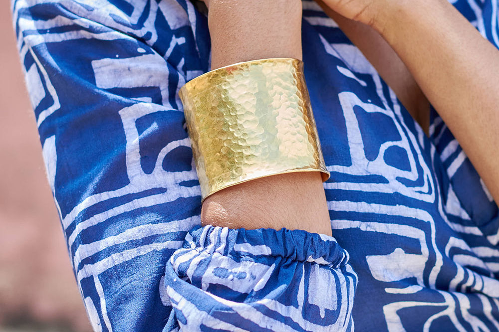 Close-up of woman wearing blue hand-dyed batik Coco print long sleeve wrap top by GEOMETRIC and brass bracelet. 
