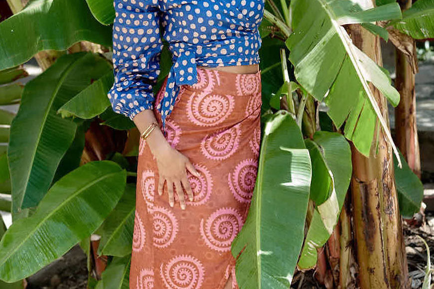 Woman wearing blue hand-dyed polka dot batik print wrap top and sea shell print wrap skirt by GEOMETRIC. 