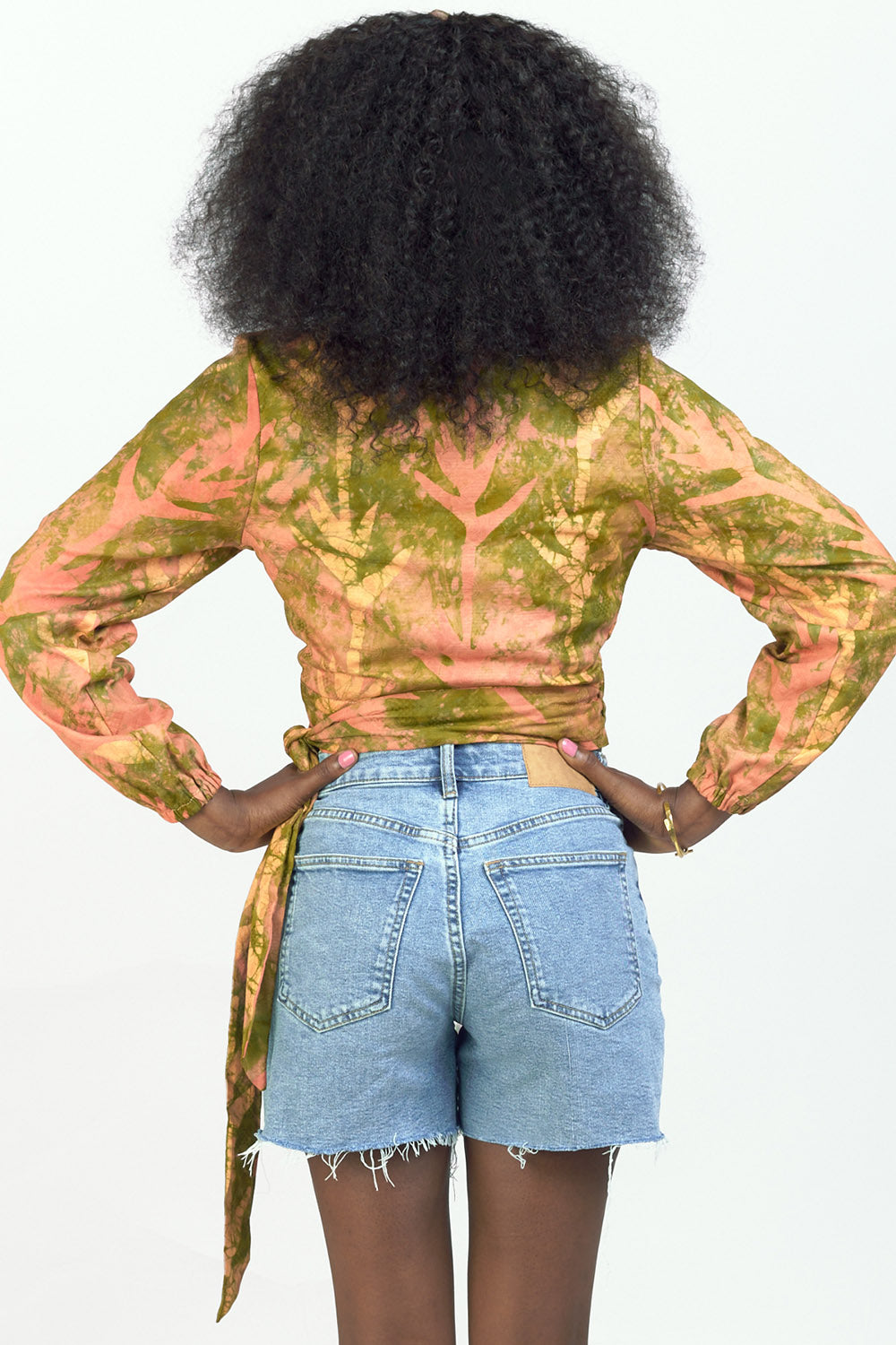 Back view of woman wearing hand-dyed orange Birds of Paradise batik print long sleeve wrap top by GEOMETRIC. 