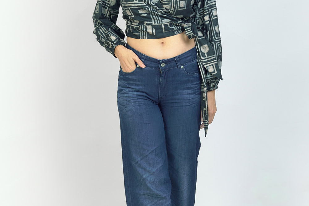 Woman wearing jeans and charcoal hand-dyed batik Coco print long sleeve wrap top by GEOMETRIC. 