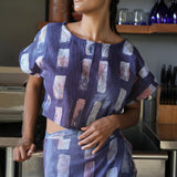 Woman standing in kitchen wearing matching crop wrap top and wrap skirt by Geometric made from purple tone hand dyed deadstock fabric. 