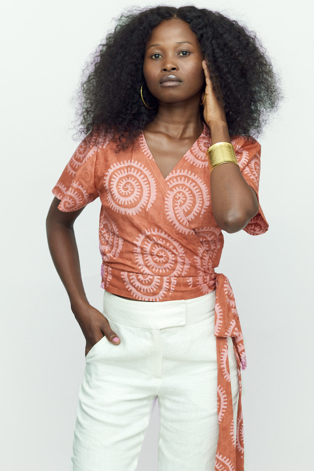 Woman wearing hand-dyed pink and orange Shea Shell dot batik print Short Sleeve Wrap Top by GEOMETRIC. 