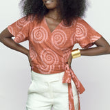 Woman wearing hand-dyed pink and orange Shea Shell dot batik print Short Sleeve Wrap Top by GEOMETRIC. 