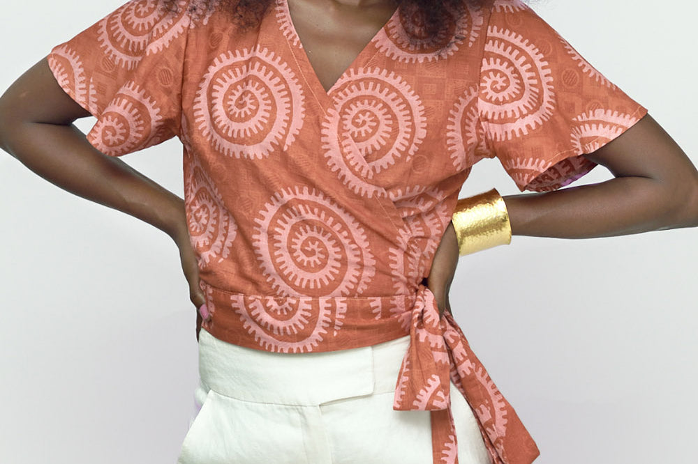 Woman wearing hand-dyed pink and orange Shea Shell dot batik print Short Sleeve Wrap Top by GEOMETRIC. 