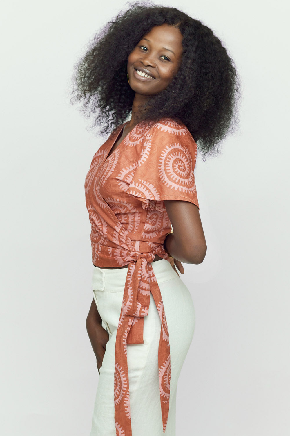 Woman wearing hand-dyed pink and orange Shea Shell dot batik print Short Sleeve Wrap Top by GEOMETRIC. 