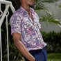 Man wearing blue shorts and hand-dyed purple Coco batik print short sleeve button up shirt by GEOMETRIC. 