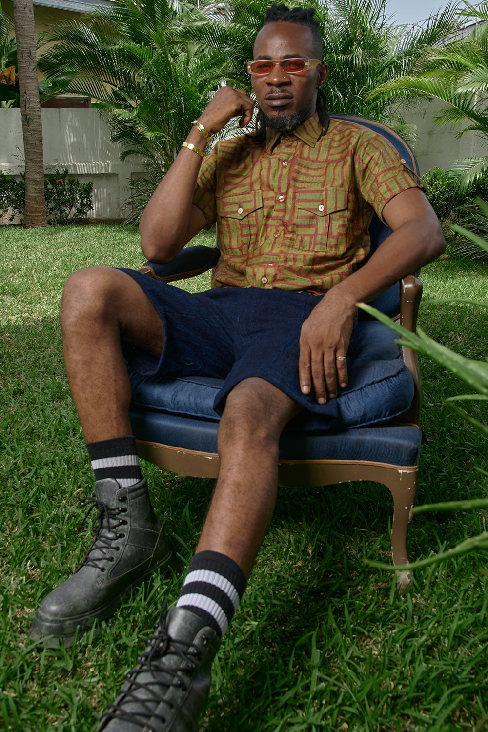 Man sitting in chair wearing hand-dyed green batik Garden Gate print short sleeve button up shirt by GEOMETRIC. 