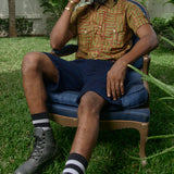 Man sitting in chair wearing hand-dyed green batik Garden Gate print short sleeve button up shirt by GEOMETRIC. 
