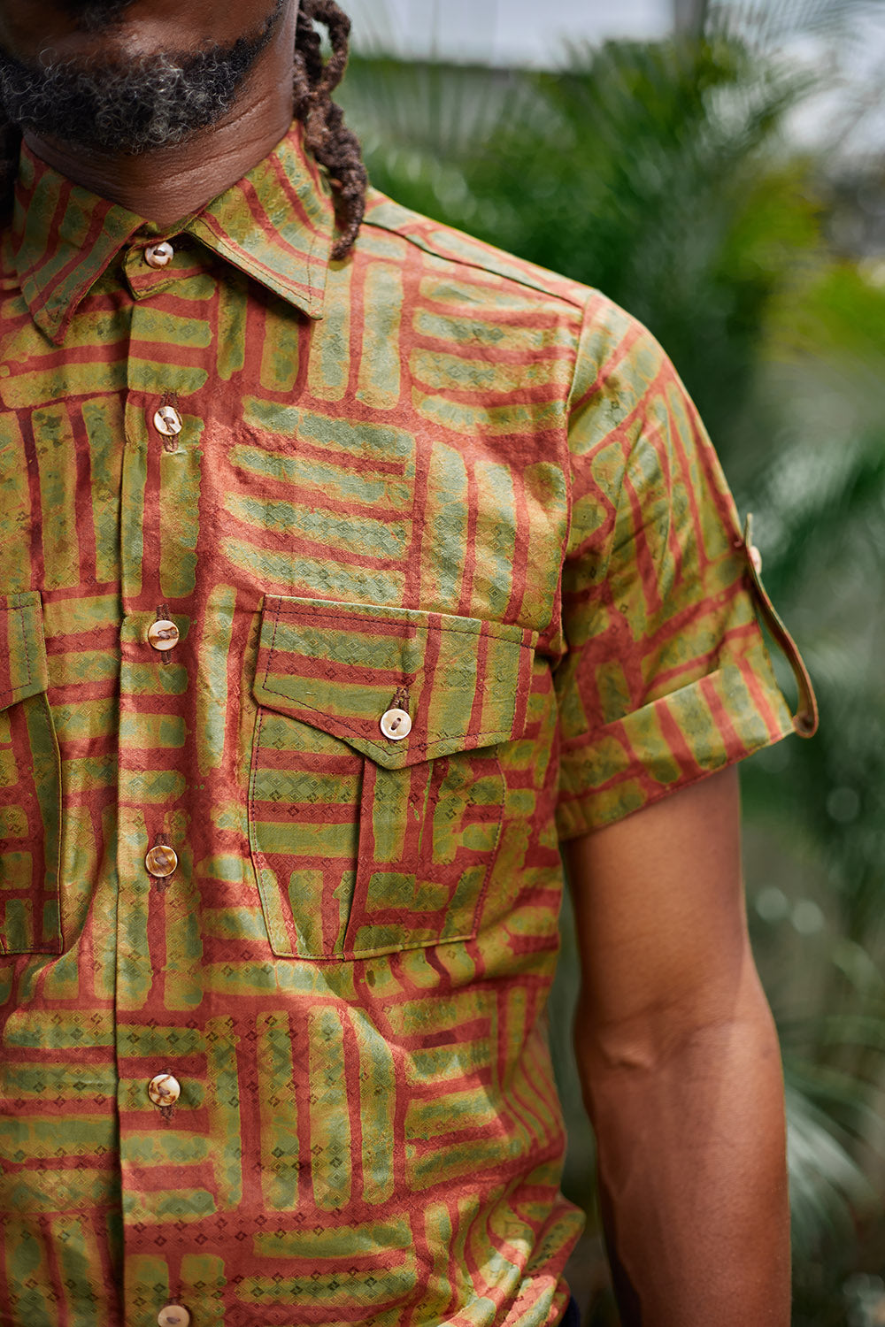 Close-up of man wearing hand-dyed green batik Garden Gate print short sleeve button up shirt by GEOMETRIC. 