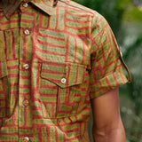 Close-up of man wearing hand-dyed green batik Garden Gate print short sleeve button up shirt by GEOMETRIC. 