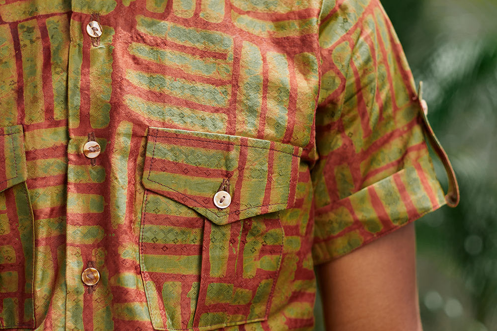 Close-up of man wearing hand-dyed green batik Garden Gate print short sleeve button up shirt by GEOMETRIC. 
