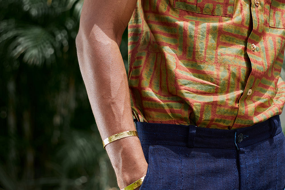 Man wearing blue shorts and hand-dyed green batik Garden Gate print short sleeve button up shirt by GEOMETRIC. 