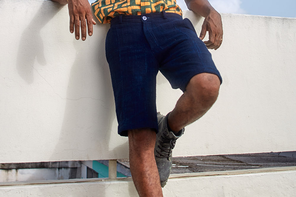 Man wearing blue shorts and hand-dyed green and gold batik print short sleeve button up shirt by GEOMETRIC. 