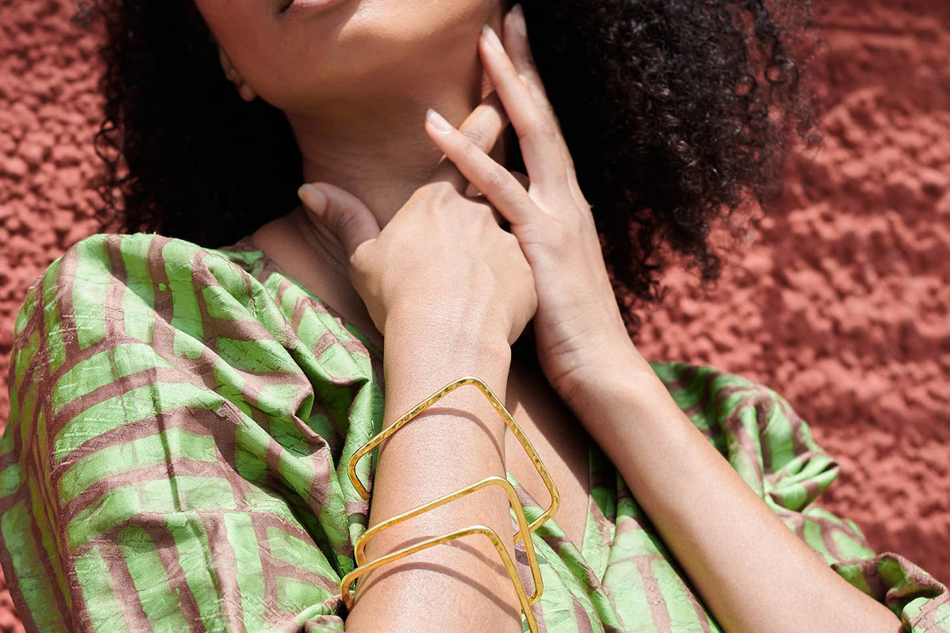 Woman wearing green wrap shirt and 3 hammered brass square shape bangle by GEOMETRIC. 