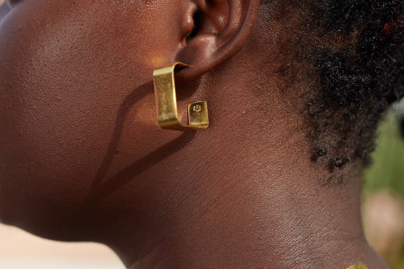 Woman wearing brass square hoop earrings by GEOMETRIC. 