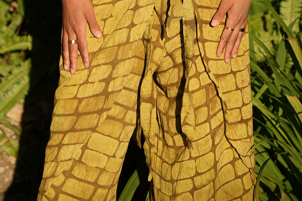 Woman wearing yellow hand-dyed batik print Technno wrap pants by Geometric. 