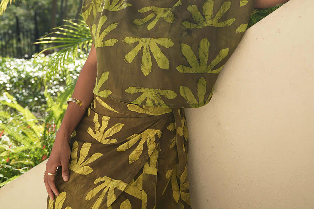 Woman leaning up against a wall wearing wrap skirt and matching top by Geometric. Skirt is made from deadstock fabric hand-dyed in green tone Sunshine print. 