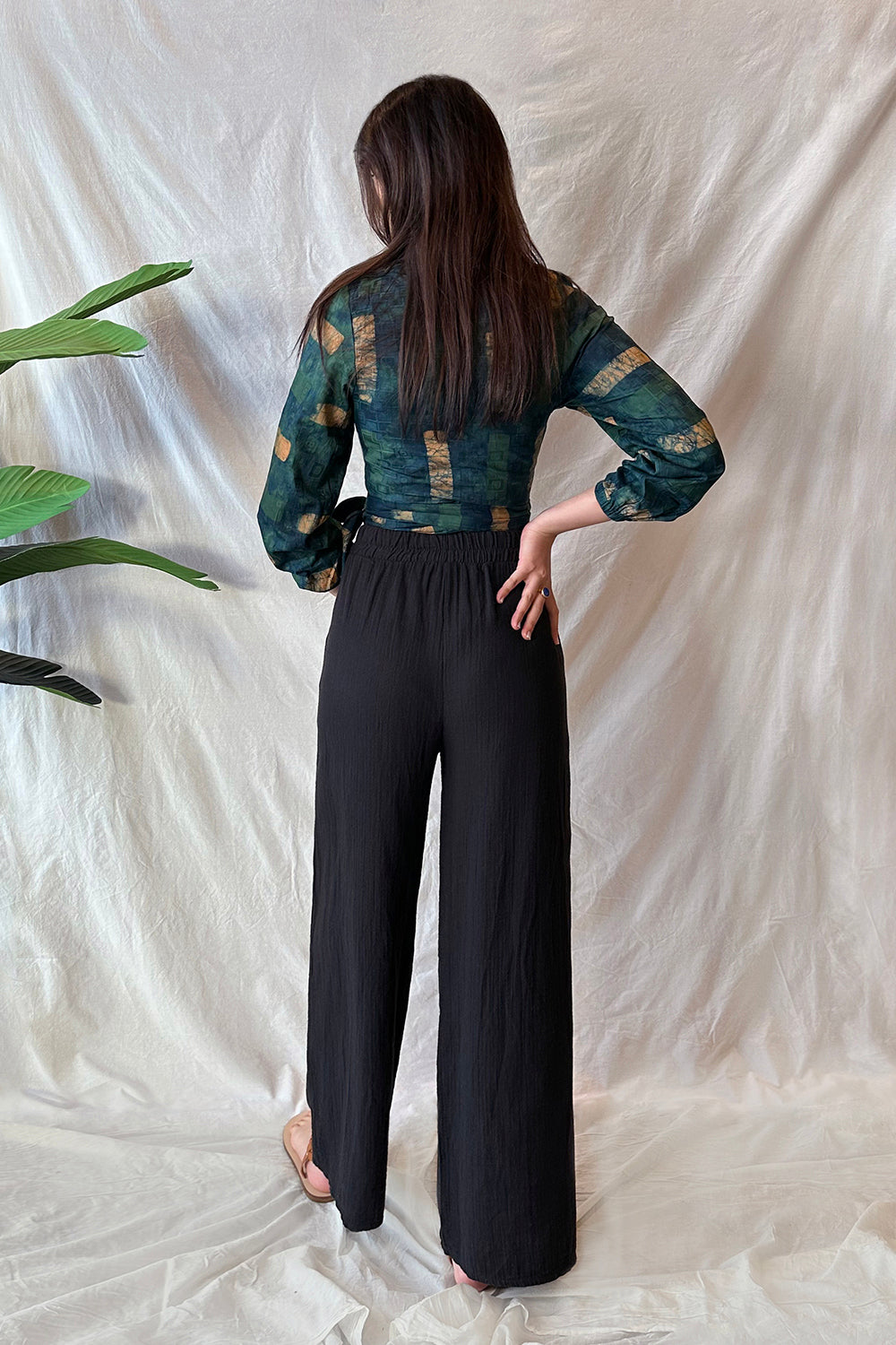 Back view of woman wearing black pants and navy hand-dyed batik Brush Strokes print long sleeve wrap top by GEOMETRIC. 