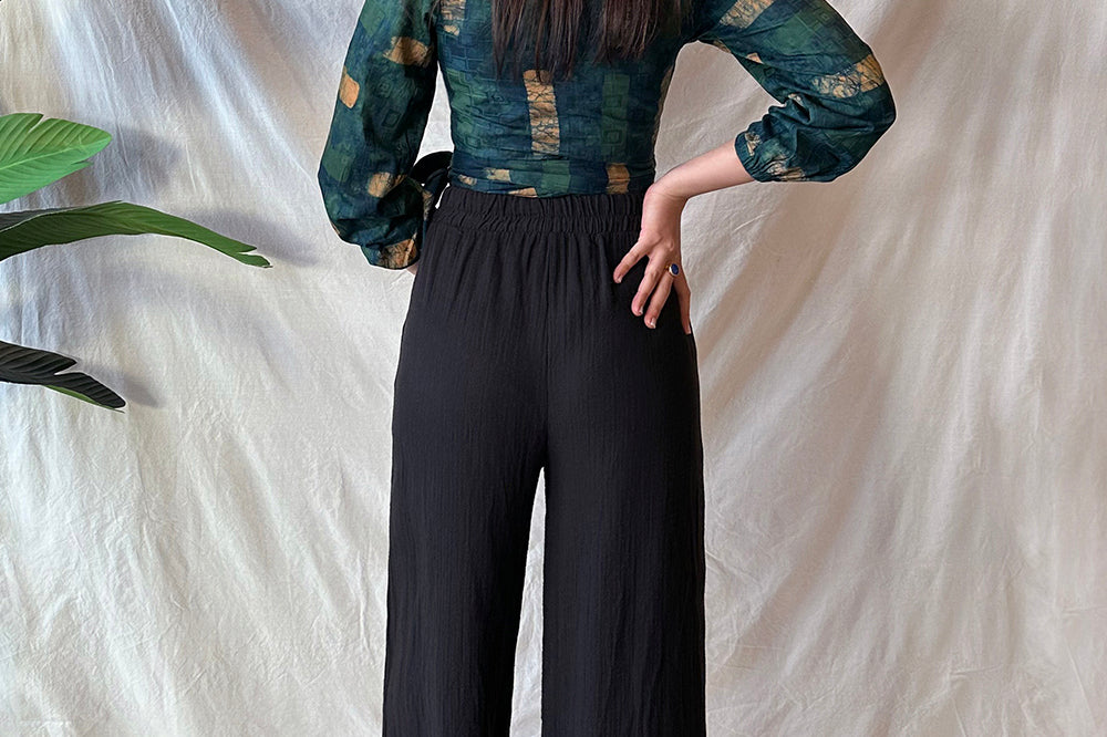 Back view of woman wearing black pants and navy hand-dyed batik Brush Strokes print long sleeve wrap top by GEOMETRIC. 