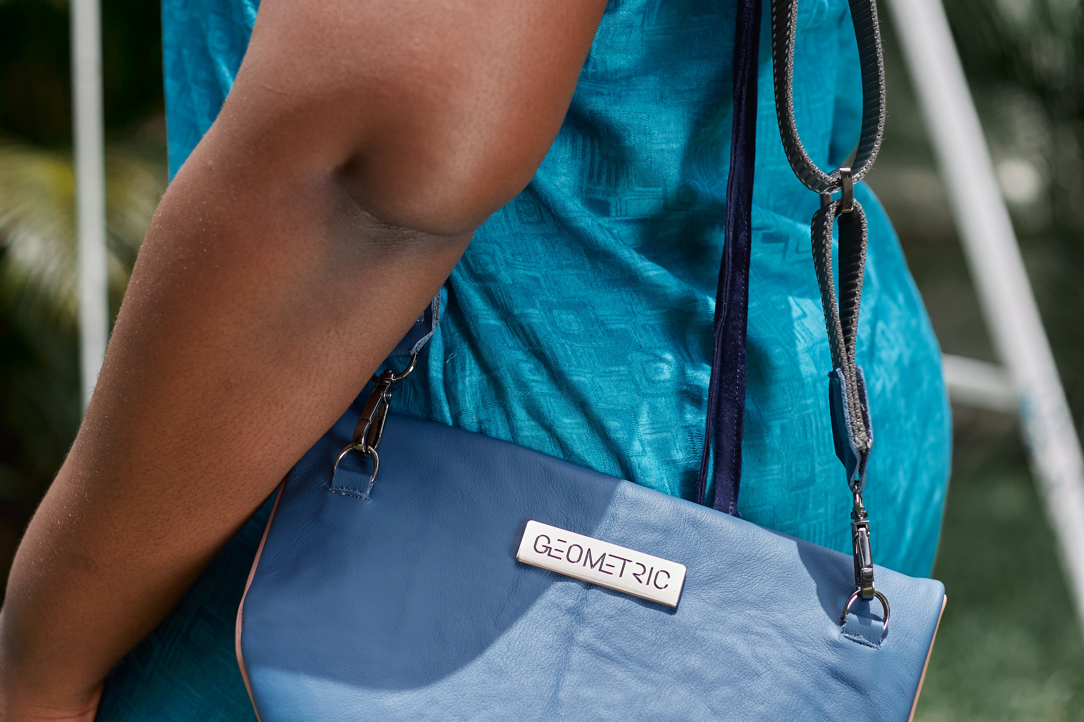 Close-up of woman carrying stone blue and pick leather Crescent cross-body bag by GEOMETRIC. 